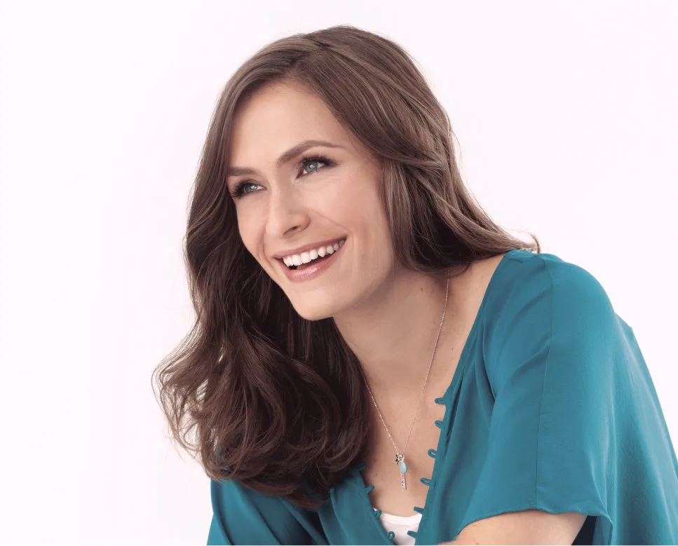 Image-3.jpg A woman with long brown hair laughs broadly in a teal blouse and a necklace.
