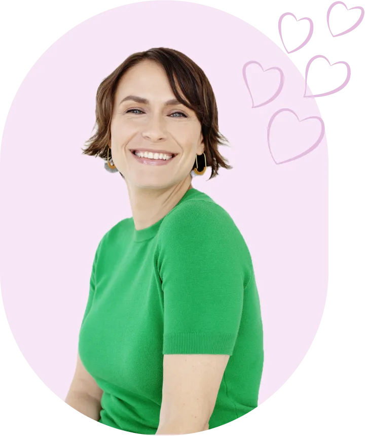 Group+13.png Smiling person in a green shirt with heart illustrations on a pink background.