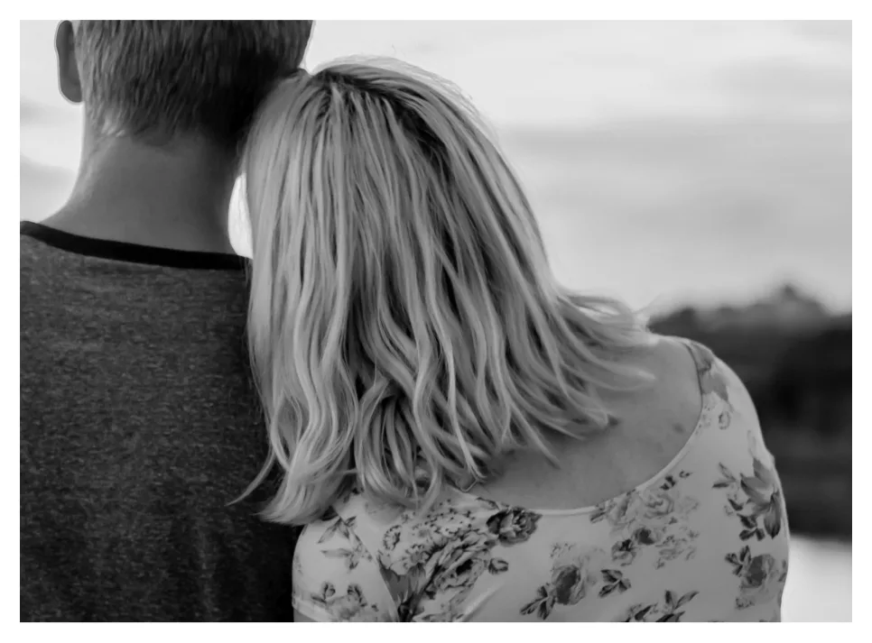 Image-13.png Black-and-white photo of a couple from behind, her head resting on his shoulder as they look out over the water.